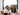 image of cofounders sitting on couch in front of a window with trees in the background, Lisa dark haired woman in 30's wearing white shirt and black pants, and Katrina blonde haired woman also in 30s wearing black shirt and white pants smiling at camera