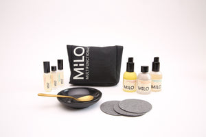 three mini sized (10ML) glass bottles with black lids, three 30ML sized product bottles with black lids, a black canvas product bag with milo multifunctional on it, 3 face sponges, a black bowl and gold spoon in the bowl