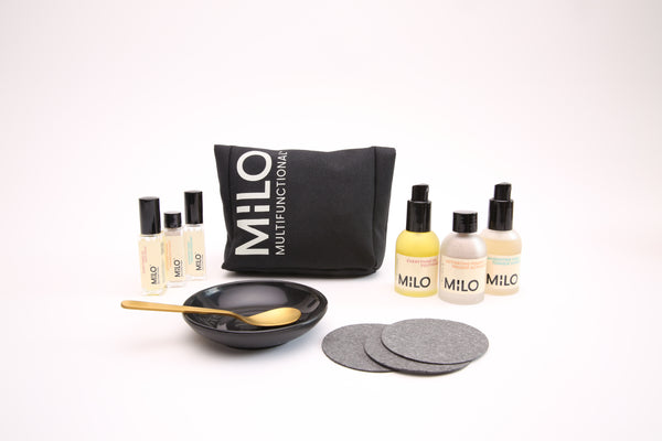 three mini sized (10ML) glass bottles with black lids, three 30ML sized product bottles with black lids, a black canvas product bag with milo multifunctional on it, 3 face sponges, a black bowl and gold spoon in the bowl