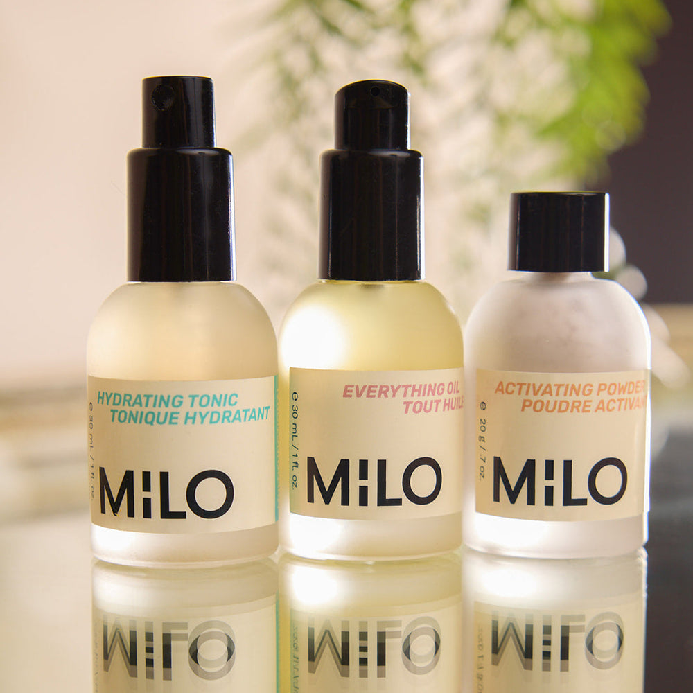 three milo products in a row, frosted bottles with black lids, hydrating tonic in turquoise font with black milo logo, everything oil in pink font with black milo logo, activating powder in orange font, with black milo logo written on bottle labels